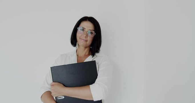 Teacher with glasses and big folder in hands smiling at camera on background
