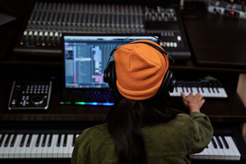 Portrait of beautiful young brunette, female artist playing keyboard synthesizer, sitting in recording studio - obrazy, fototapety, plakaty