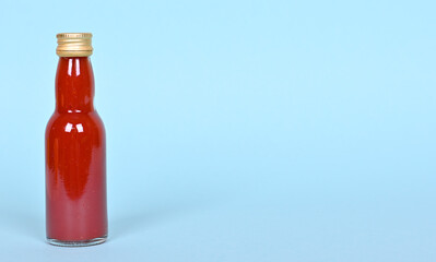 Hot red chilly sauce in little glass bottle on blue background.
