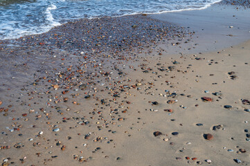 Colorful pebbles on the sand by the sea, in the background small waves, horizontal orientation
