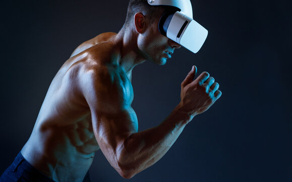 Muscular model sports young man in glasses of virtual reality on dark background. Fashion portrait of strong brutal guy. Sexy torso. Male flexing his muscles. VR. Blue neon light.