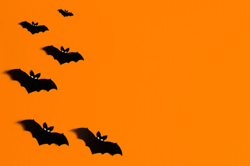 orange background with a flock of black paper bats for Halloween, black paper bat silhouettes on an orange background, Halloween concept, copyspace, flatlay, top view, overhead