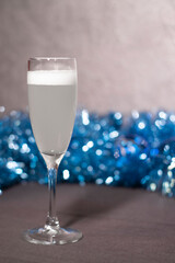 glass of champagne near blue tinsel for Christmas tree.