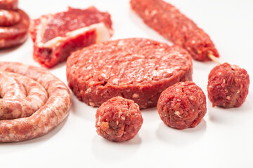 Close-up on raw meatballs, patty, sausage and kebab on white bac