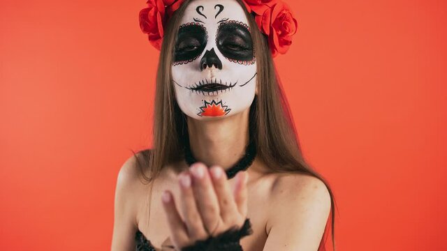 Day of Dead, woman with sugar skull make-up smiling and sending you an air kiss posing on red background, Halloween
