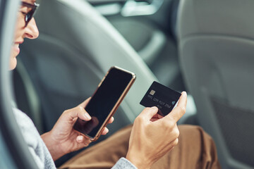 Close up shot of smiling business woman using her smartphone and credit card to buy something while sitting on back seat in the car