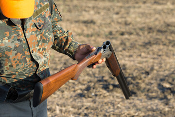 Duck hunter with shotgun walking through a meadow.