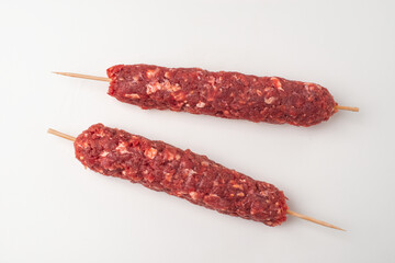 Minced beef meat on wooden skewers on white background