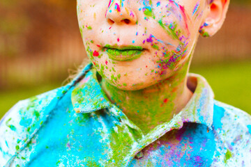 happy boy painted with Holi festival colours having fun in autumn park