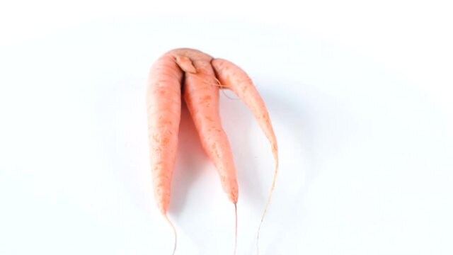 Ugly carrot rotate on a white background. Funny, unnormal vegetable or food waste concept. Horizontal orientation