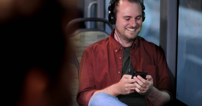 Man holding smartphone sitting inside bus listening music on headphones