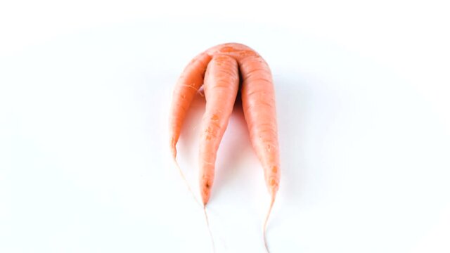 Ugly carrot rotate on a white background. Funny, unnormal vegetable or food waste concept. Horizontal orientation