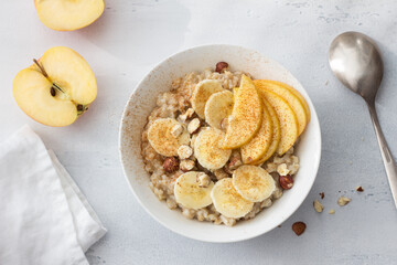 Delicious healthy breakfast. Oatmeal with banana, apple, nuts and cinnamon on a light gray background, top view	