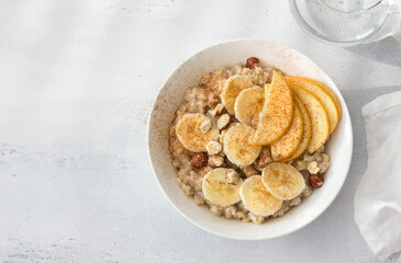 Delicious healthy breakfast. Oatmeal with banana, apple, nuts and cinnamon on a light gray background, top view, space