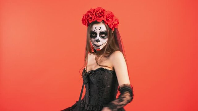 Day of Dead, lady with sugar skull make-up dancing, performing curtsy and smiling posing on red background, Halloween