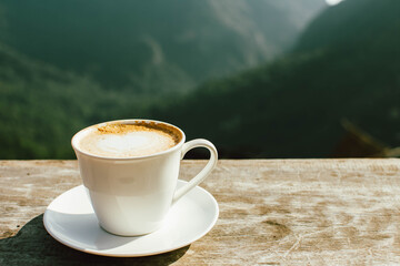 Hot latte coffee in winter morning at hillside with mountain background. Copy space for text.
