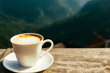 Hot latte coffee in winter morning at hillside with mountain background. Copy space for text.
