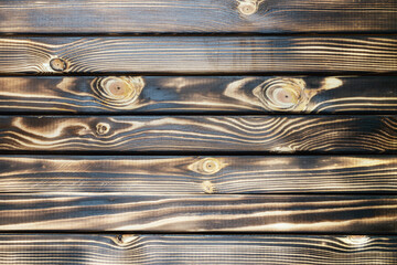 Old burnt wooden plank dark brown texture background with horizontal boards. Flat lay close-up view.