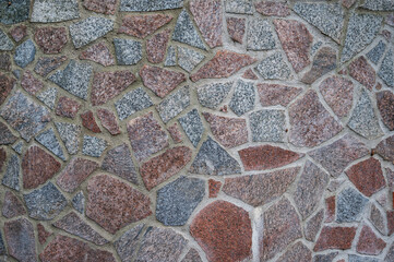 Background wall of red and gray granite pieces of stones fastened with cement, horizontal orientation