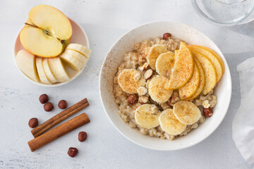 Delicious healthy breakfast. Oatmeal with banana, apple, nuts and cinnamon on a light gray background, top view	