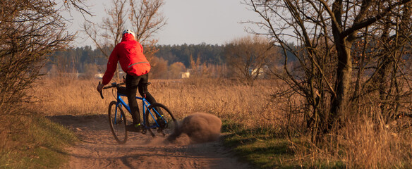 Cyclist on a gravel bike rides along the road raising dust from the rear wheel at sunset. Gravel...