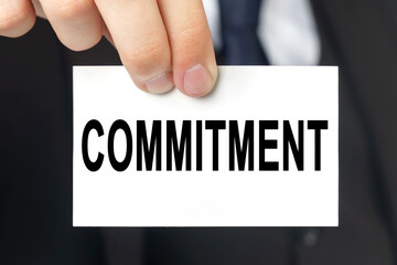 Businessman shows a card with the text - COMMITMENT