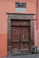 Quito, Ecuador - December 2, 2008: Historic downtown. Brown dilapidated sculpted door as entrance to Public Library, Maroon wall as backdrop.
