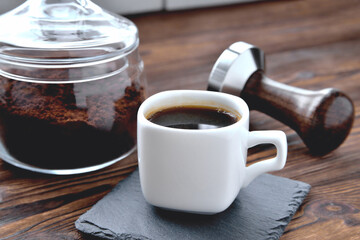 coffee in a cup on a stone stand, glass jar with coffee beans and coffee tamper, wooden natural background