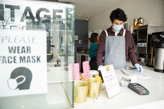 Male barista in face mask working at cafe counter