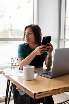 Thoughtful young female cafe owner using smart phone at table