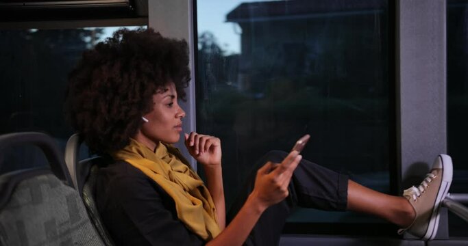 African-american woman with earphones and smartphone sitting on public bus