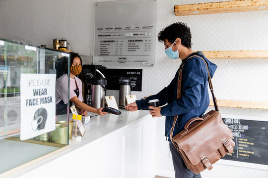 Young man in face mask paying barista with smart card in cafe