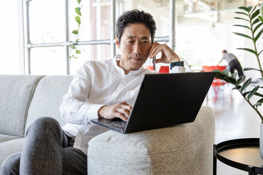Man using laptop on sofa in business coworking space