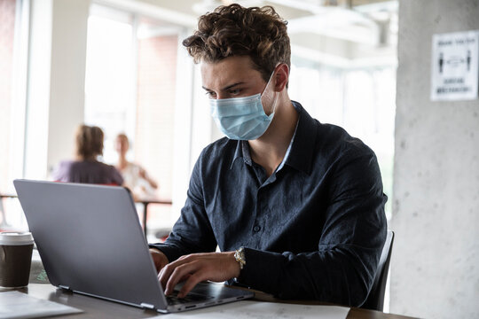 Designer in face mask using laptop in socially distanced space