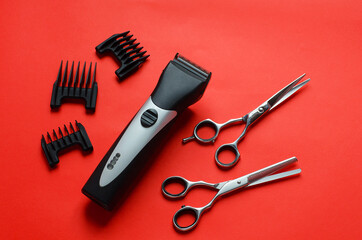 Fototapeta premium Barber clipper,scissors for haircuts,nozzles for haircuts on a red background.Free space for text.Barber tool.New year at the hairdresser.Discounts and promotions for the new year.New Years hairstyles