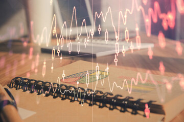 Double exposure of financial graph drawings and desk with open notebook background. Concept of forex market
