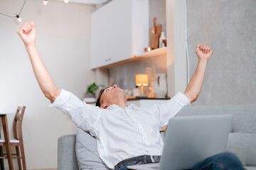 Obraz premium happy young man with a laptop is celebrating sitting on the sofa.