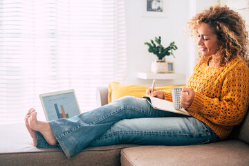 Beautiful single woman work at home with paper book and computer laptop together in old and modern job style concept - people in smat working sitting on the sofa and not in traditional office