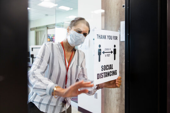 Teacher Sticking Social Distancing Poster On Class Door