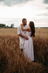 Stock photo portrait of bearded boyfriend hugging his gorgeous girlfriend both in white clothes hugging in wheat field. Beautiful wheat field in the background.