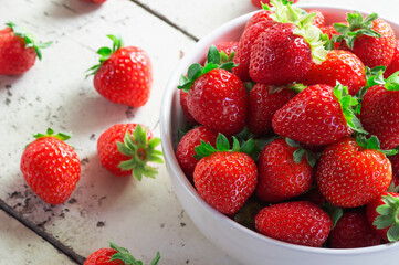 Fresh ripe harvested strawberries in bowl on white wooden table, Summer fruit, strawberry ( Fragaria )