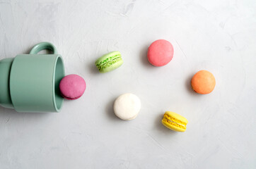 many multicolored crunchy delicious macarons dropped out of a ceramic cup on a gray concrete background. morning coffee concept. sweets and desserts.