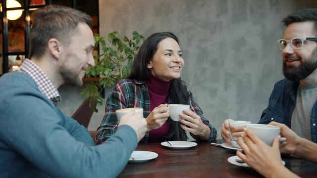 Joyful friends male and female are talking and drinking coffee enjoying leisure time together at table in cafe. Modern lifestyle and people concept.