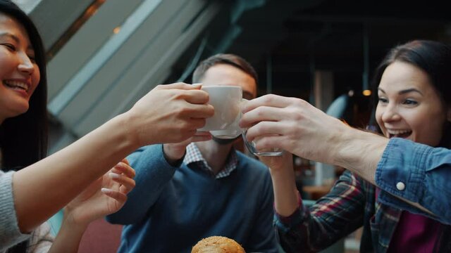 Slow motion of happy friends men and women celebrating event in cafe clinking coffee cups laughing having fun together. People and celebrations concept.