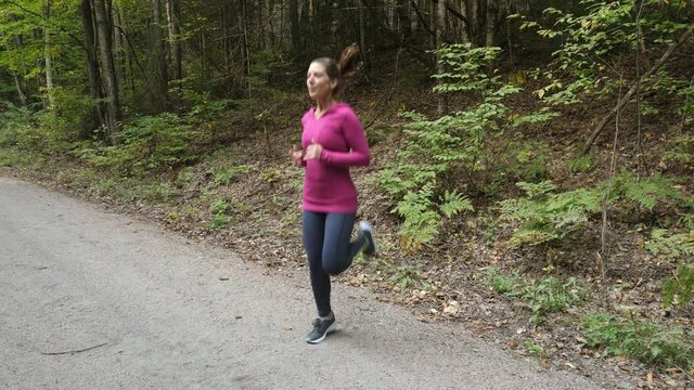 Athletic 40s woman running on spot. Warming up. Forest trail.