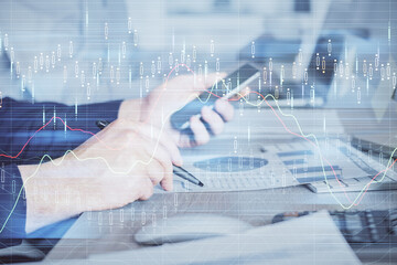 Double exposure of man's hands holding and using a digital device and forex graph drawing. Financial market concept.