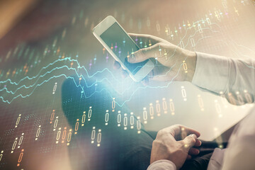 Double exposure of man's hands holding and using a digital device and forex graph drawing. Financial market concept.
