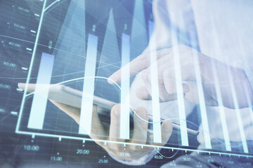 Double exposure of man's hands holding and using a digital device and forex graph drawing. Financial market concept.