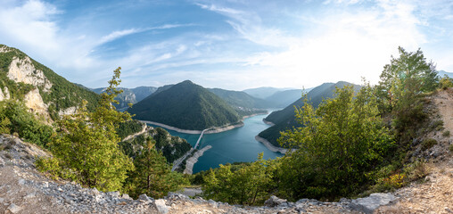 Lovely panorama of Lake Piva or Pivsko jezero in Montenegro. View to the bridge from Durmitor to Pluzine town and mountains under the blue sky with clouds.