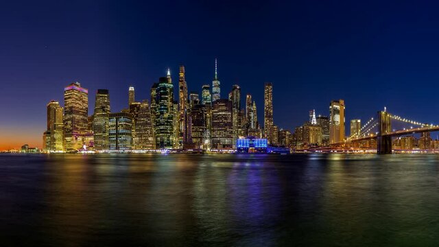 Panoramic image of lower Manhattan and the Brooklyn Bridge at night with the Hudson river reflecting the lights.